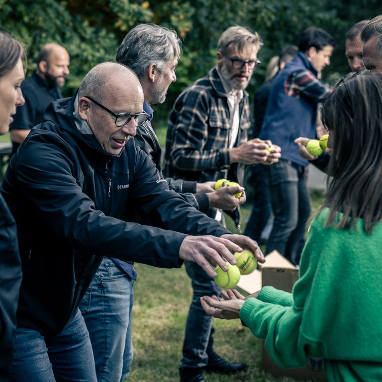 Deelnemers geven elkaar tennisballen door tijdens een teamoefening op een Beanmachine-dag